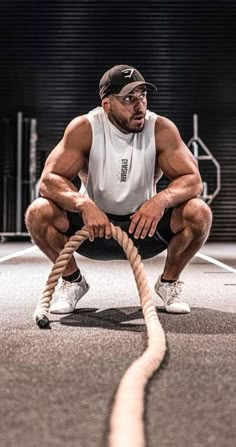 a man squatting down while holding a rope