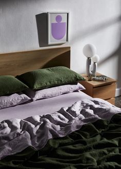 a bed with green and white pillows in a bedroom next to a lamp on a nightstand