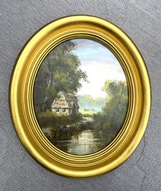 an oil painting of a house by a river in a gold frame on a gray background