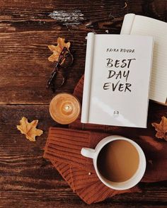 an open book sitting on top of a wooden table next to a cup of coffee