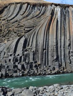 a large rock formation next to a body of water with waves coming out of it