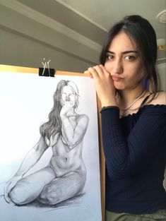 a woman is holding up a drawing in front of her face and looking at the camera