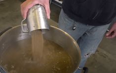 a man is pouring something into a large metal pot with water in it and his hands are on the side of the pan