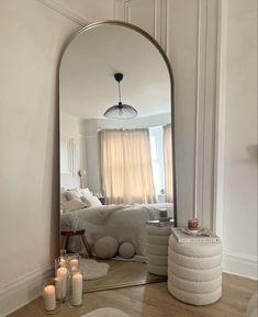 a large mirror sitting on top of a wooden floor next to a white bed in a bedroom