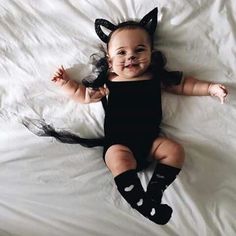 a baby dressed up as a cat laying on top of a white sheet covered bed