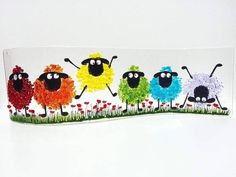 a group of colorful sheep standing on top of a grass covered field in front of a white wall