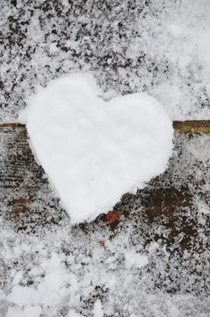 a heart - shaped piece of white snow on top of a wooden table covered in snow