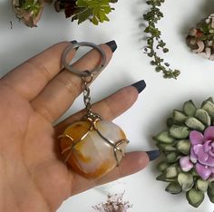 a hand holding a keychain in front of various plants and flowers on a table