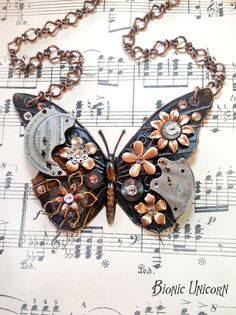 a butterfly shaped necklace with music notes and flowers on it's back, sitting on top of sheet music