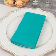 a white plate topped with a blue napkin next to flowers and candles on top of a table