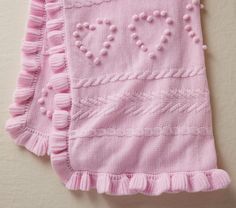 a pink knitted blanket with ruffles and beads hanging on a white wall