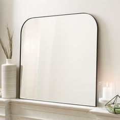 a mirror sitting on top of a mantle next to a vase