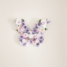 a butterfly made out of flowers sitting on top of a white wall next to a vase