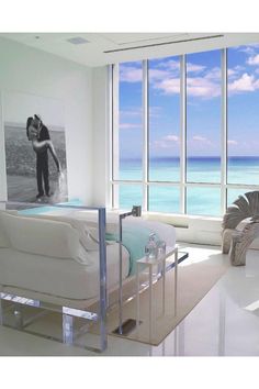 a living room filled with white furniture and large windows overlooking the ocean on a sunny day