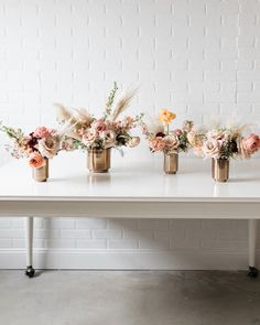 three vases with flowers are sitting on a white table in front of a brick wall