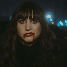 a woman with blood all over her face and mouth, standing in the dark at night