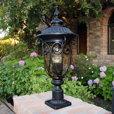 an old fashioned street light sitting on top of a brick table in front of some flowers