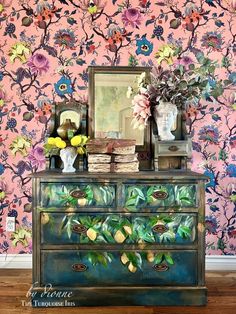 a dresser with flowers painted on it in front of a pink wallpapered background