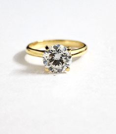 a yellow gold engagement ring with a round diamond in the center, on a white background