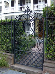 an iron gate in front of a house with flowers and bushes on the side walk