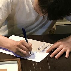 a person writing on a piece of paper at a table with a pen in their hand