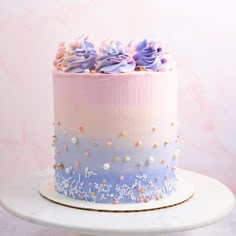 there is a pink and blue cake with flowers on the top, sitting on a white plate