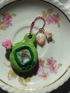 a green frog keychain sitting on top of a white plate with pink flowers