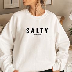 a woman wearing a white sweatshirt with the word salty printed on it in black letters