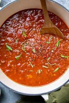 a wooden spoon in a pot filled with red sauce and garnishes on the side