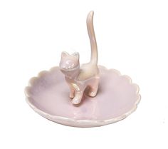 a white cat figurine sitting on top of a pink bowl with scalloped rim