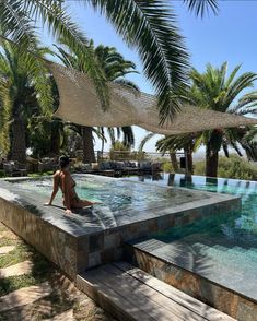 a woman sitting on the edge of a swimming pool in front of some palm trees