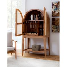 a wooden shelf with bottles and glasses on it in front of a white wall next to a chair