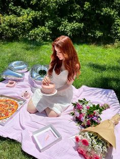 a woman sitting on a blanket with pizza and flowers in front of her, holding a cake