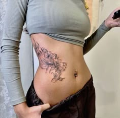 a woman with a tattoo on her stomach holding a cell phone and looking at the camera