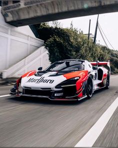 a red and white sports car driving down the road in front of a bridge overpass