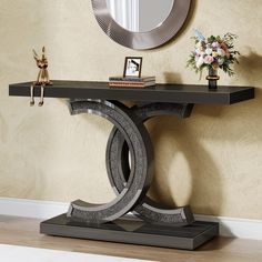 a black console table with a mirror on the wall behind it and a vase filled with flowers