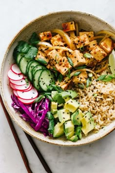 a bowl filled with rice, cucumber, radishes and tofu