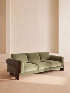 a green couch sitting on top of a hard wood floor next to a white wall