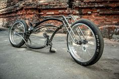 a bike that is sitting on the ground in front of a brick wall with wheels attached to it