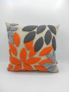 an orange and grey decorative pillow with leaves on it's side, sitting on a white surface