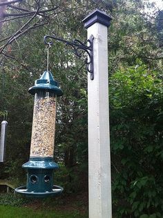 a bird feeder hanging from the side of a pole next to a tall white pole