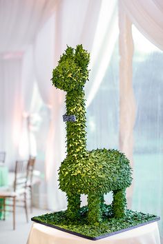 a table topped with a tall green topiary covered in leaves and an animal figure