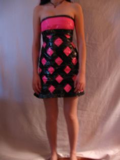 a woman standing in front of a white backdrop wearing a dress with pink and black squares on it