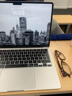 an open laptop computer sitting on top of a wooden desk next to a pair of glasses