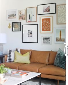 a living room filled with lots of pictures on the wall above a brown couch and coffee table