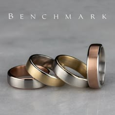 three different colored wedding bands sitting next to each other on top of a gray surface