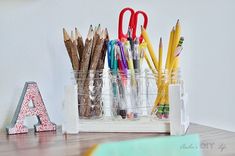 several pencils, markers, and scissors are arranged in a cup on a desk