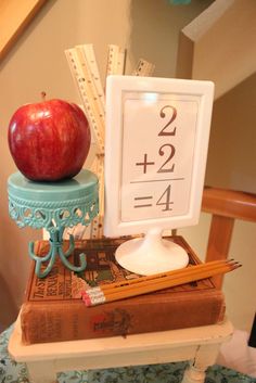 an apple sitting on top of a stack of books next to a ruler and pencils