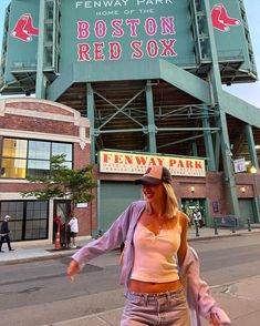 a woman walking on the sidewalk in front of fenway park with boston red sox sign