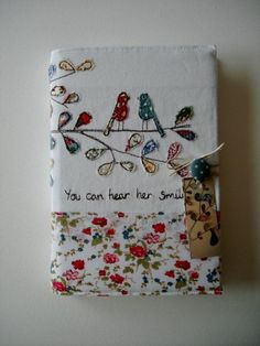 a small notebook covered in fabric with birds and flowers on the cover, which reads you can hear her smile